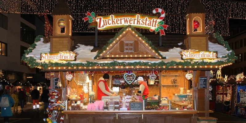 Zuckerwerkstatt Stand aus Holz bei Nacht mit leuchtender Beschriftung